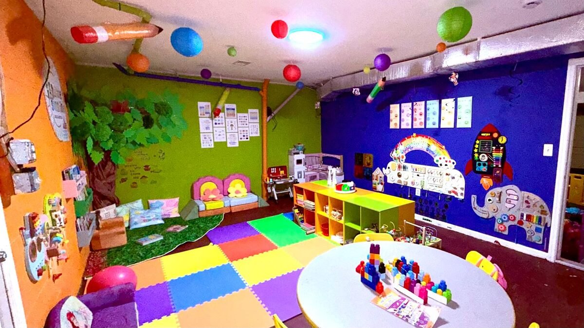 Salón principal de Little Sunshine, con piso de colores, mesa de bloques y paredes decoradas