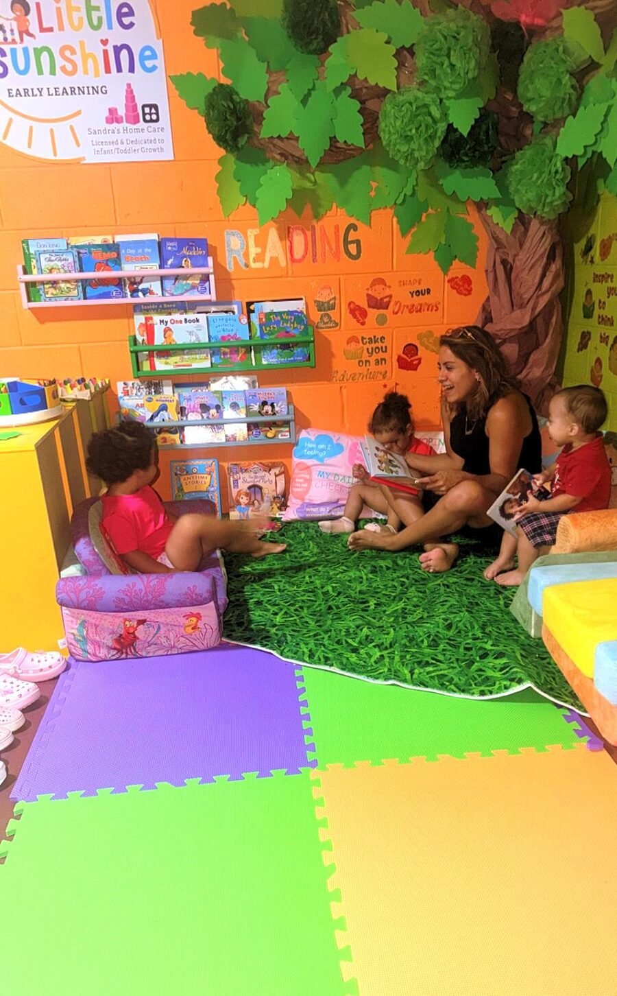 Miss Sandra leyendo cuentos con tres niños en el rincón de lectura